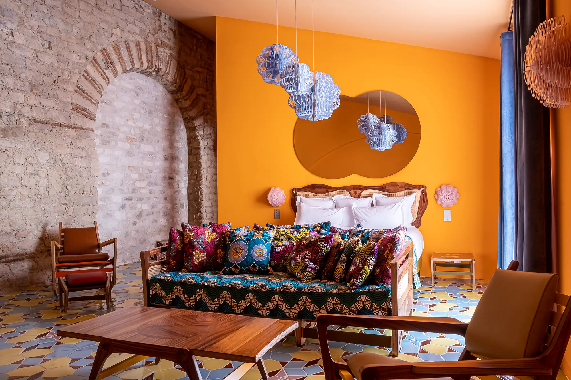 Chambre de L'Arlatan orange avec lit au centre de l'image. A gauche, un mur de pierres et une arche romane.