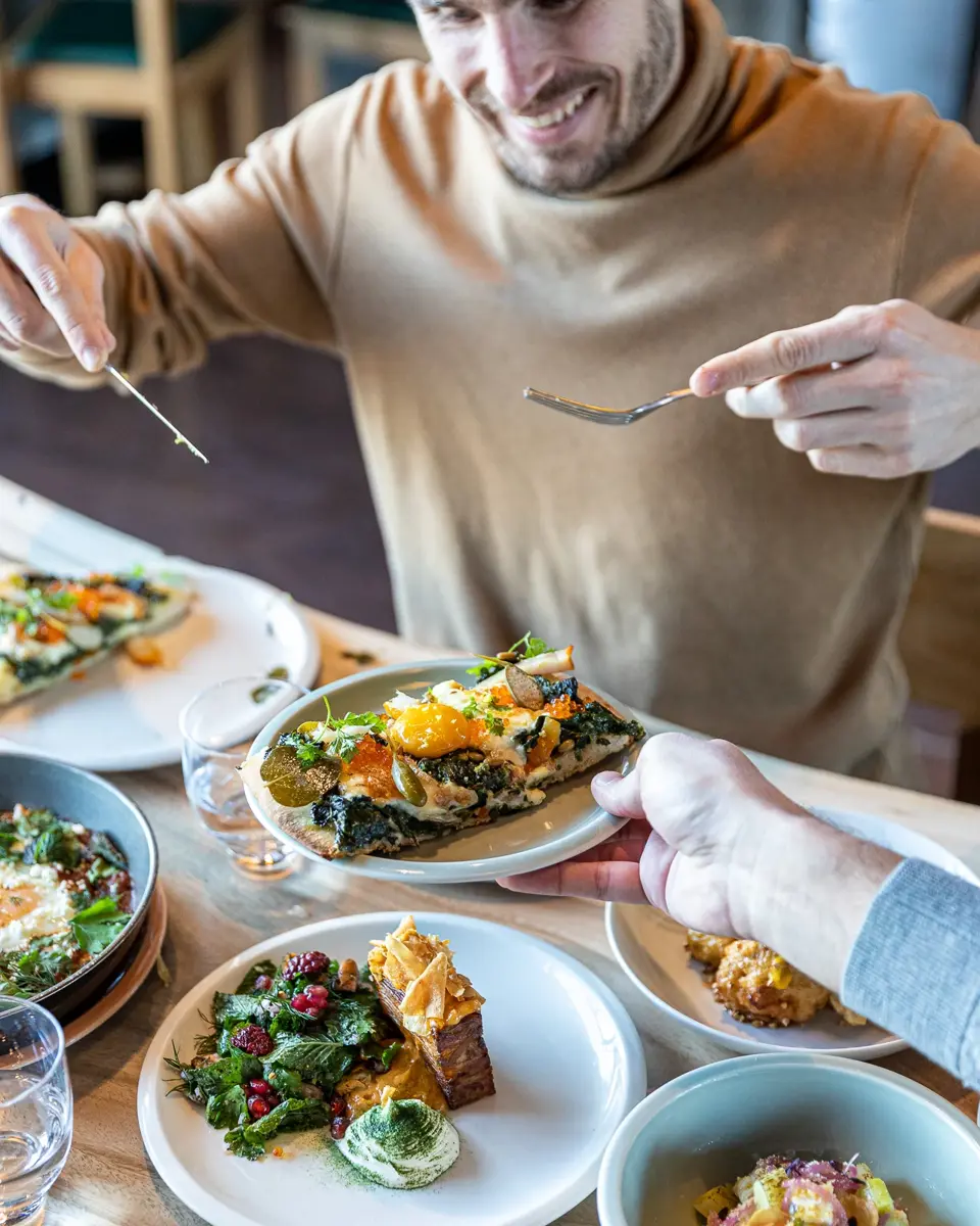Hand holding a plate above a wooden table covered with plates filled with food.