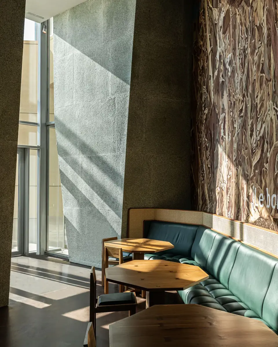 Tables en bois et banquette en cuir vert devant une tapisserie monumentale en laine de mérinos d'Arles.