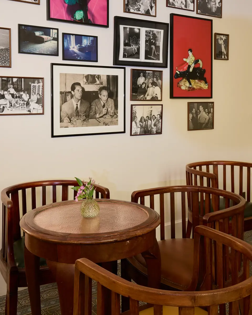 In the foreground, four wooden chairs around a copper-topped table. In the background, a wooden bar counter.