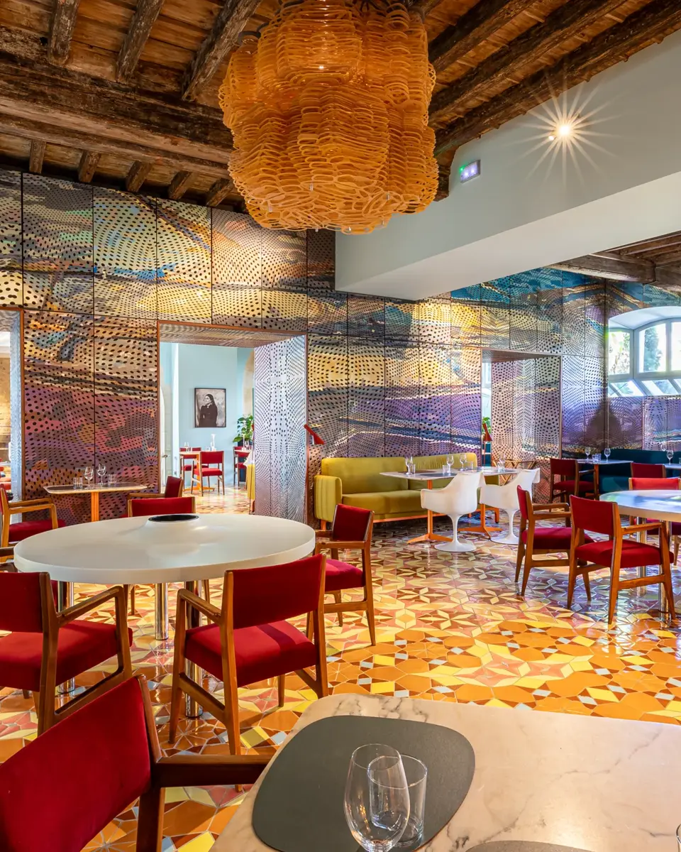 Salle de restaurant de L'Arlatan. Au premier plan, une table dressée. En arrière-plan, plusieurs tables dressées et un grand miroir qui couvre le mur reflète la salle.